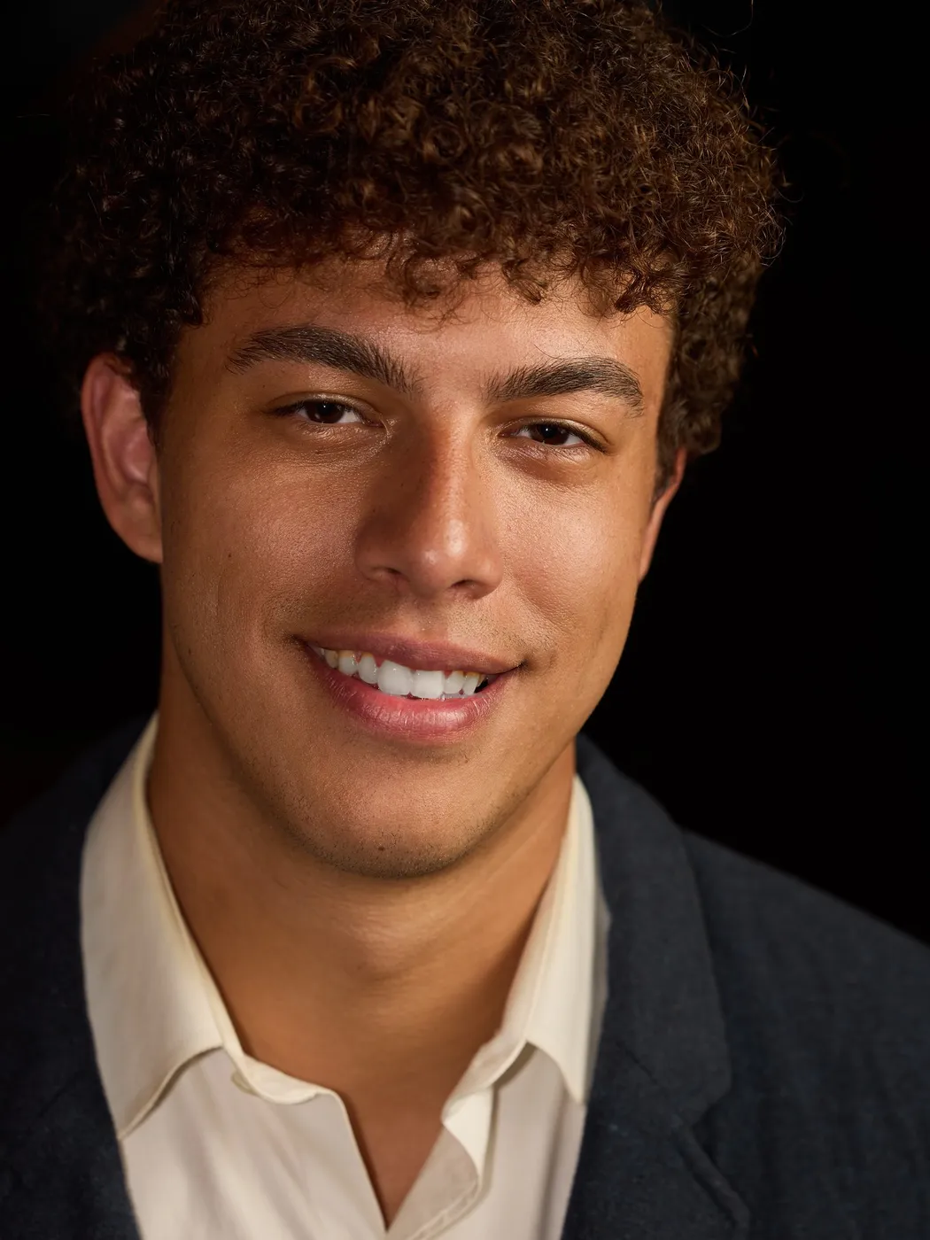 Portrait of Ethan Savage, smiling, in a cream shirt and dark blazer.
